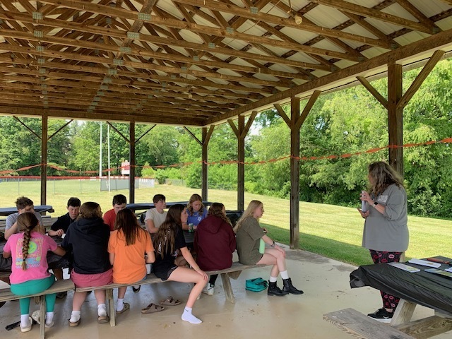A woman talks with students in a picnic shelter.