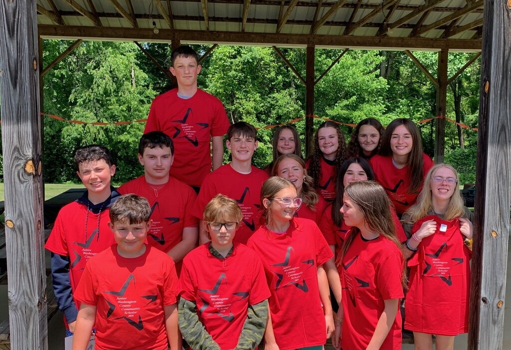 Students wearing matching red shirts pose in a picnic shelter.