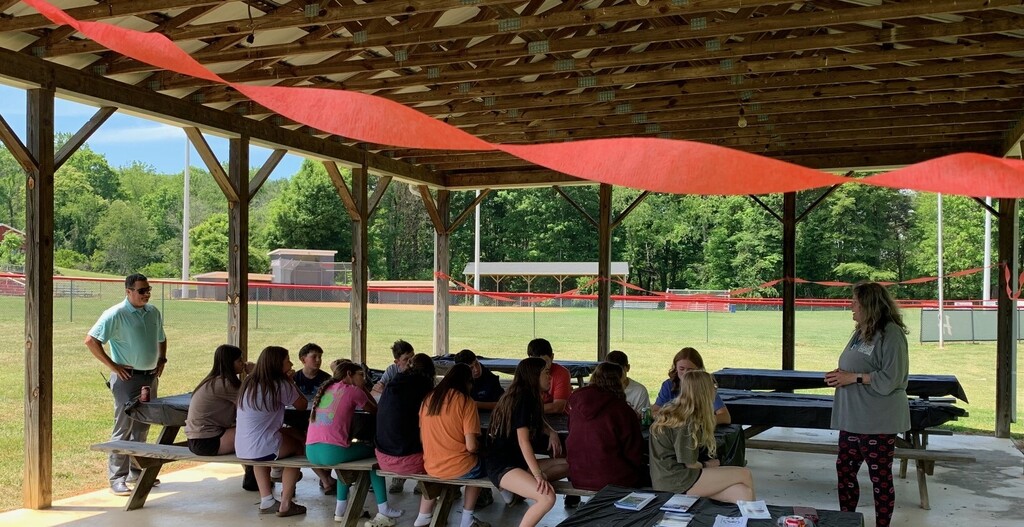A woman talks with students in a picnic shelter.