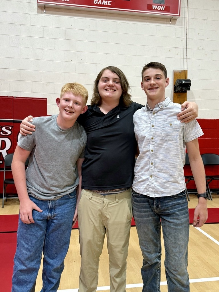 Three students stand in a gym.