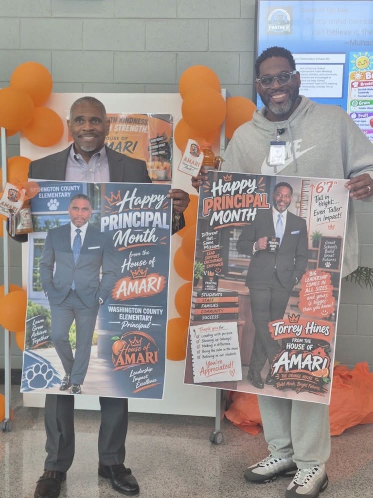 Washington County Elementary School Principal Mr. Peele (left) and Washington County High School Principal Mr. Torrey Hines (right) stand smiling during a National Principals Month celebration. Mr. Peele wears a dark suit and holds a personalized poster featuring his photograph, the words “Happy Principal Month,” and the House of Amari logo. Mr. Hines wears a gray Nike sweatsuit and holds a large poster celebrating Mr. Hines leadership and dedication. Orange balloons and House of Amari decorations fill the background, creating a festive display honoring Mr. Peele and his contributions to Washington County Elementary School.