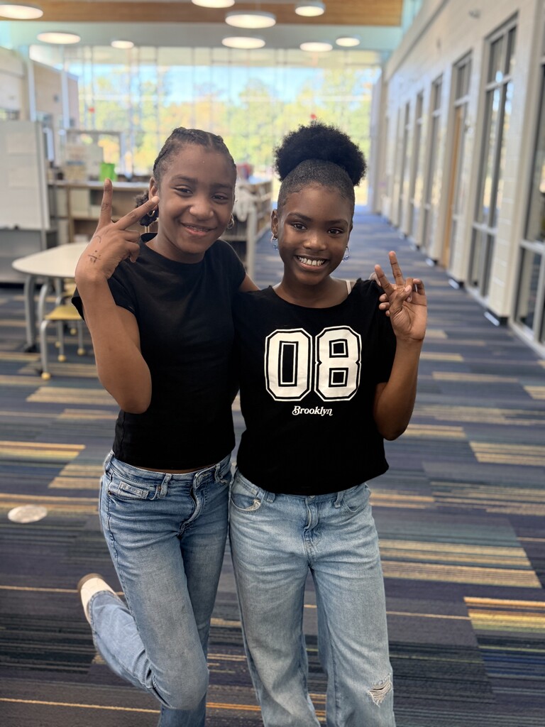 2 students wearing black shirts and jeans with peace signs.