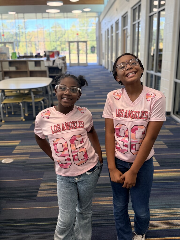 2 girls wearing pink jerseys and jeans.