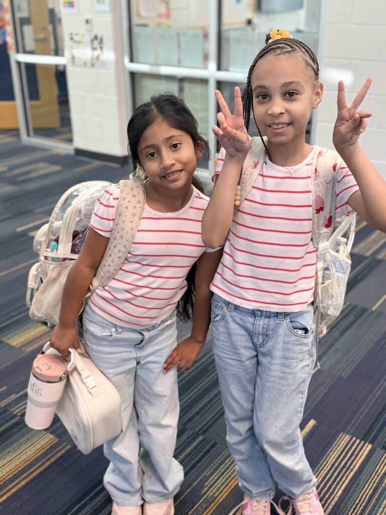 2 students wearing white and read striped shirts and jeans.