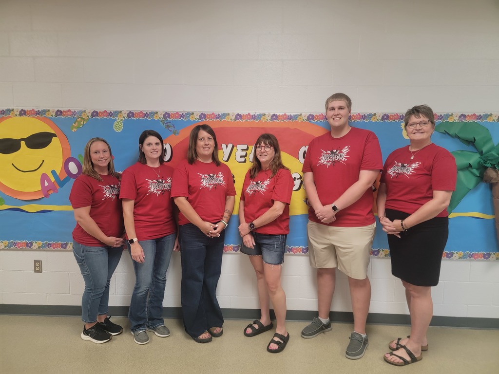 Teachers posing in front of bulletin board.