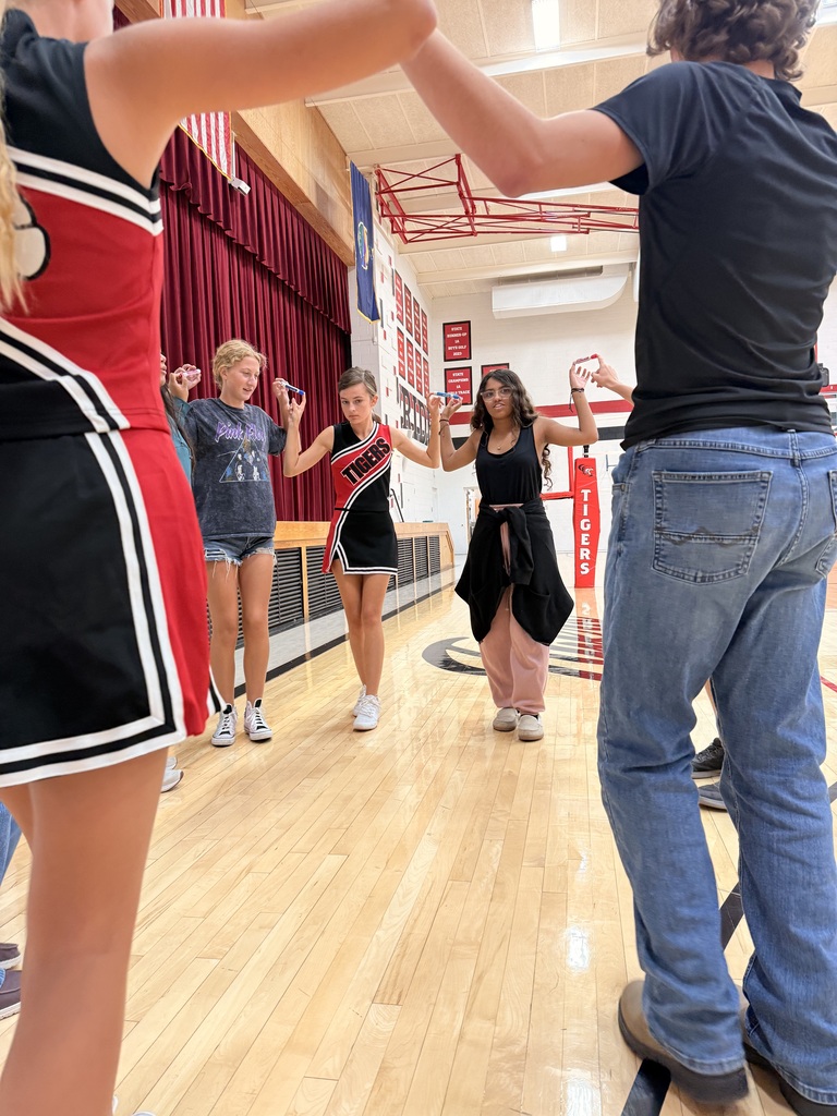 HS Cross Country runners in a circle holding expo markers between their index fingers in a race against other team representatives.