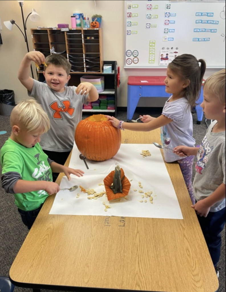 students at a table in a classroom smiling and discovering what the inside of a pumpkin looks and feels like