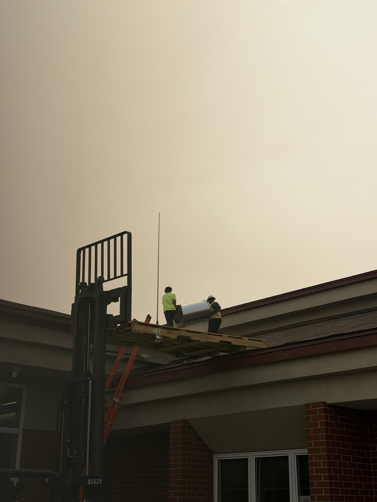 Construction workers installing equipment on the roof of Waterville School.