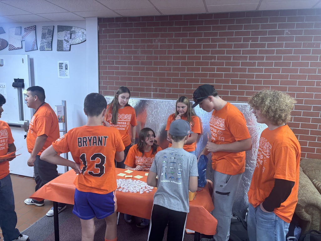 Students in orange shirts gathered around a table.