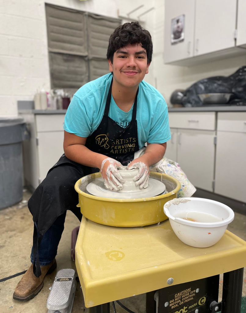 male student working on the pottery wheel with clay