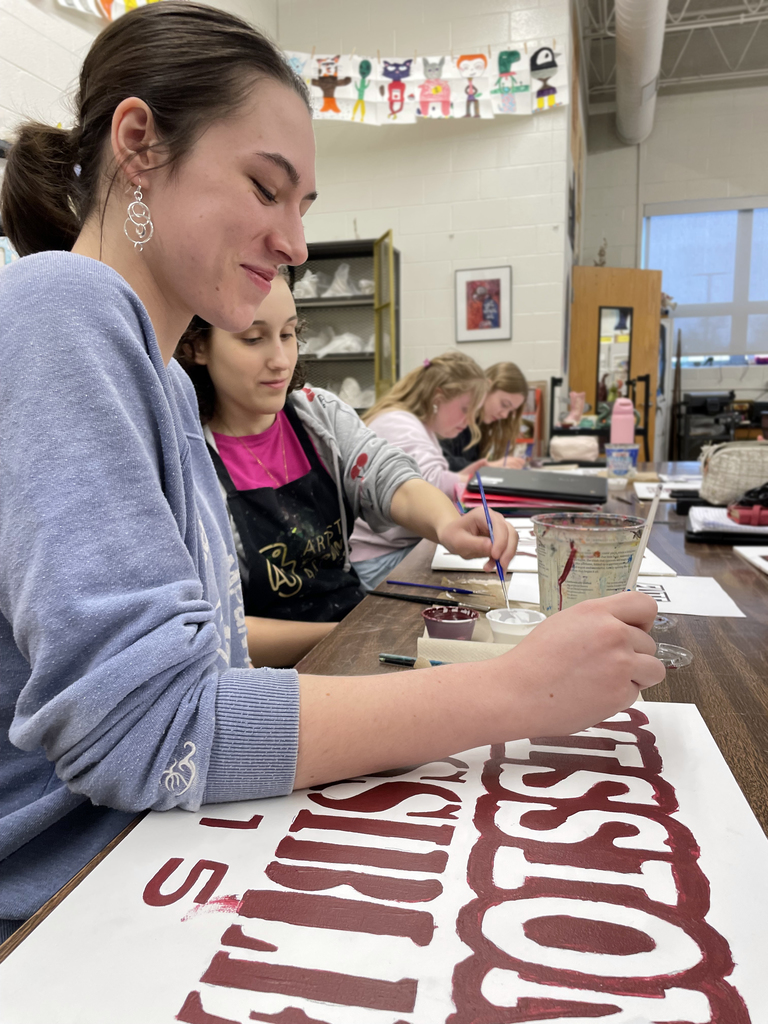 female students painting wall mural motto