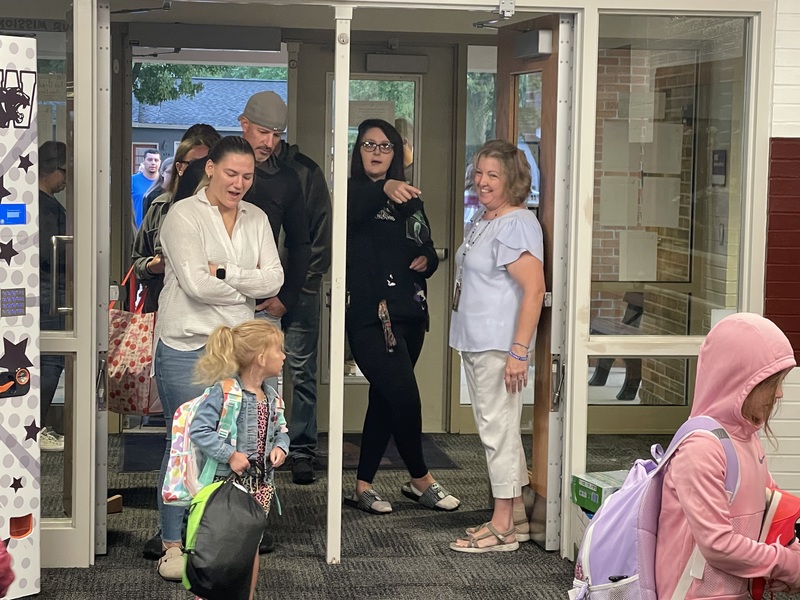 Principal and teachers greeting students at the door