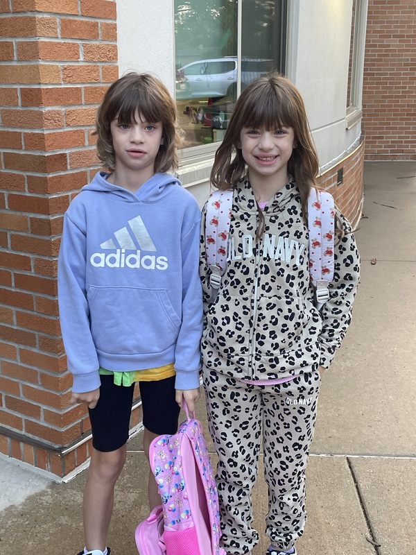two girls standing outside the school building, one holding backpack