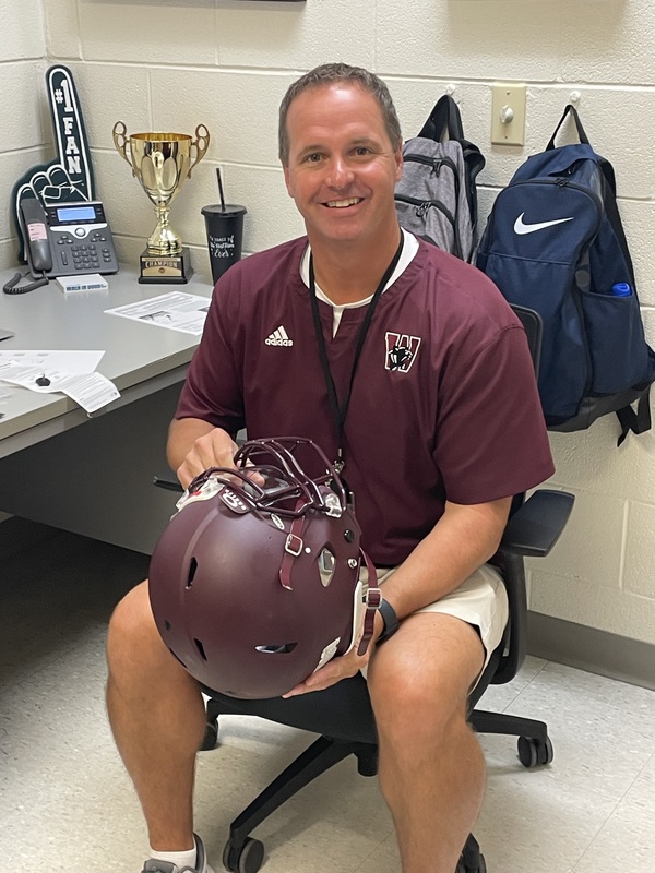 MS gym teacher sitting holding football helmet