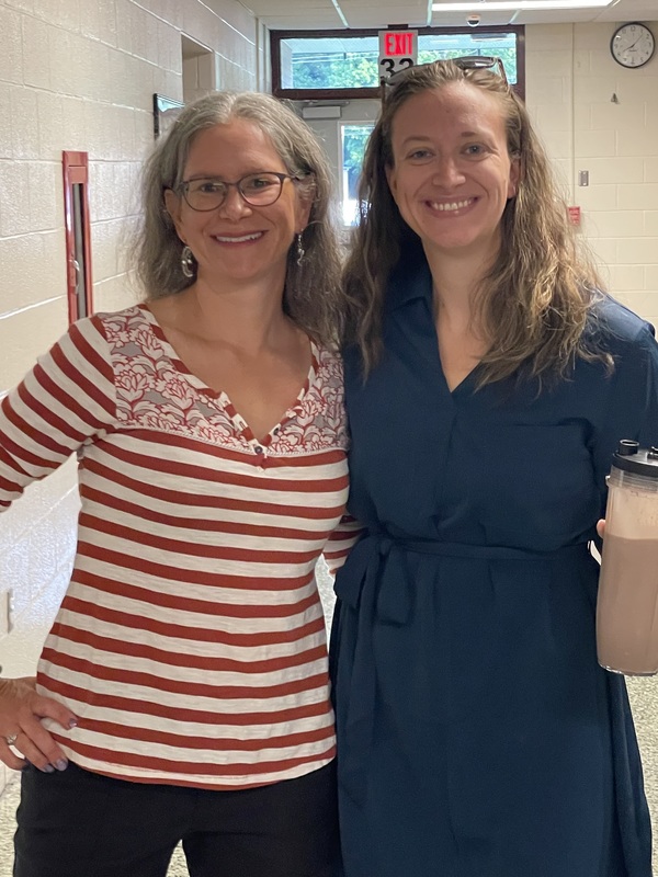 two female teachers, 1 wearing a red stripe shirt, 1 in solid green