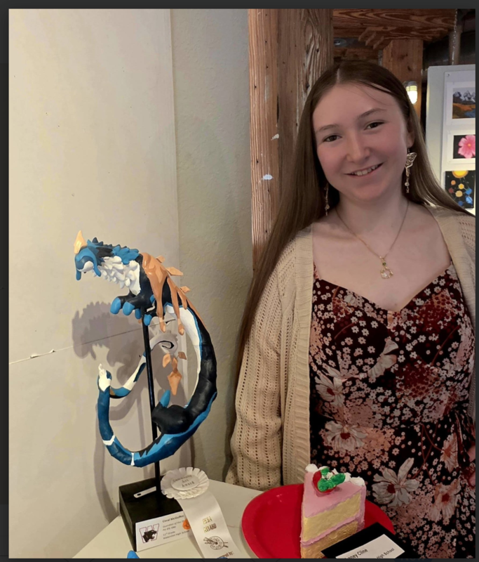 Coral McGuffey standing with her clay dragon sculpture