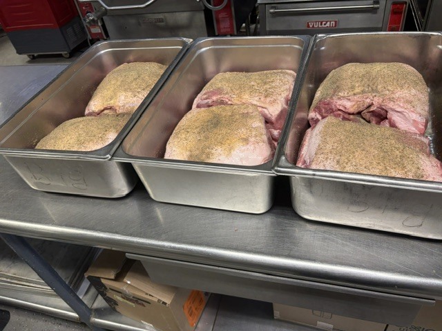 Three trays of seasoned meat sit on a kitchen counter. The meat is in large pieces and appears to be salted.