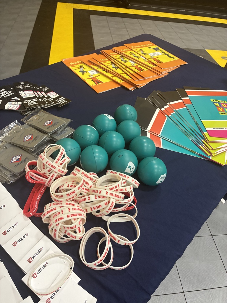 A table displays blue balls, white and red bands, and various brochures and papers on a blue cloth.