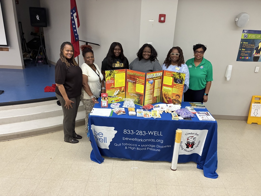 Five women stand behind a table with a blue cover. They are looking at a display of pamphlets and flyers.