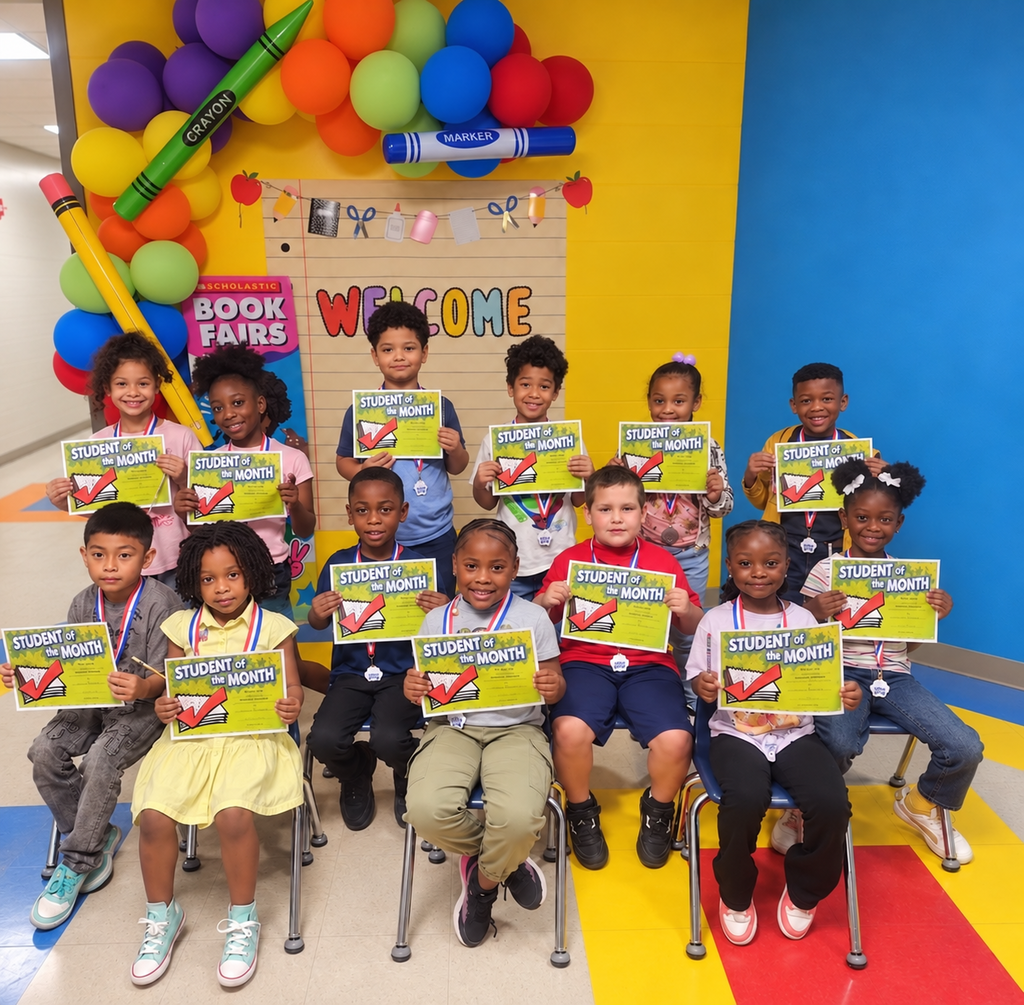 A group of children wearing medals and holding certificates. They sit in chairs in a colorfully decorated room.