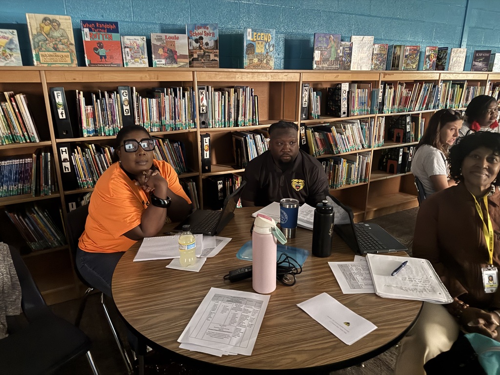 People seated around a table in a library. Some have laptops, papers, and a water bottle.