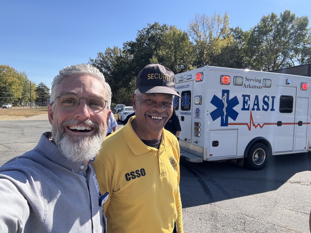 Two men stand in front of an ambulance with EASI logo, trees and parking lot in background.