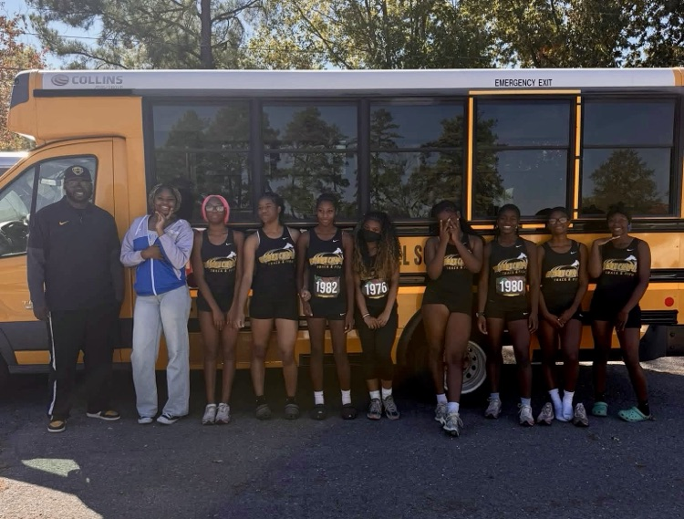 People stand in two rows in front of a school bus. The front row has two adults and five people. The second row has six people.