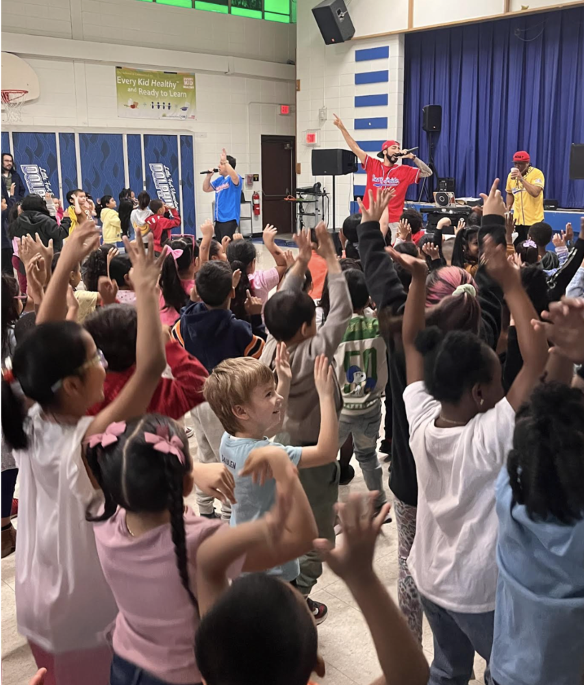 students dancing with their hands raised in the air and a DJ signing in the background