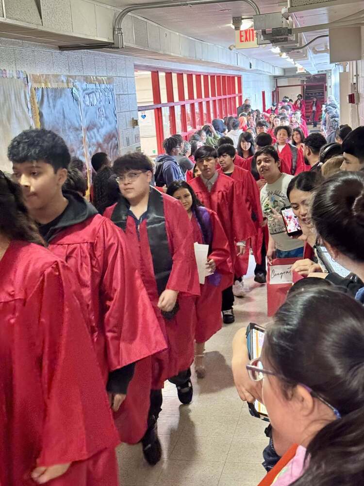 Students wearing red graduation gowns walking in a line down the hallway.
