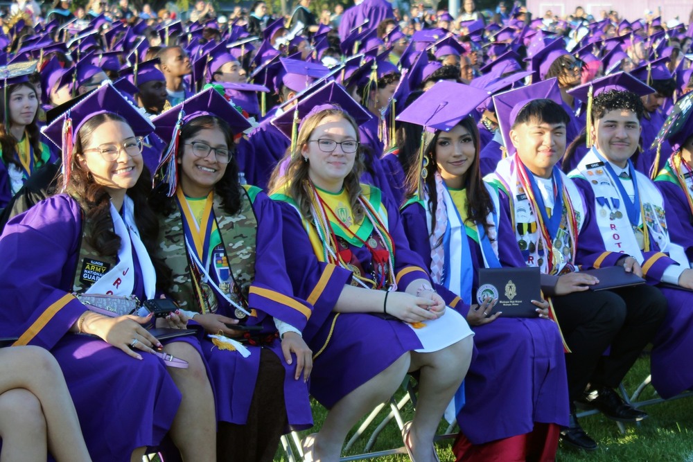 A group of high school seniors smile brightly during their graduation ceremony, dressed in their traditional caps and gowns.