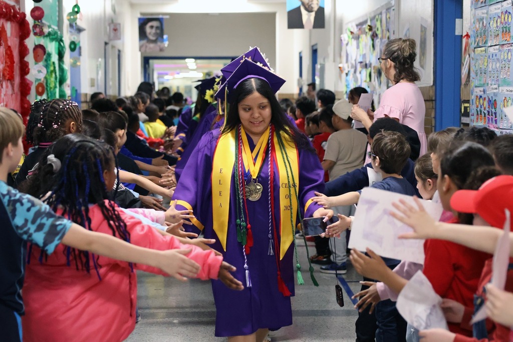 Elementary school students high-fiving and shaking hands with graduating high school seniors walking by in their caps and gowns
