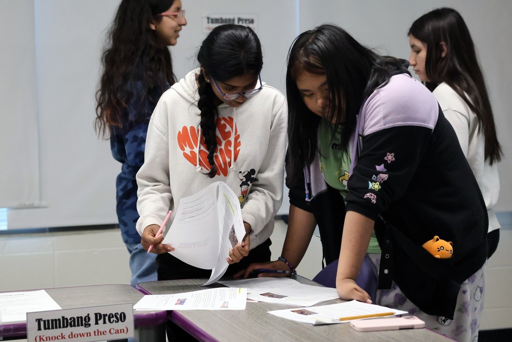 Two students sit side-by-side, looking down as they collaborate on a classroom worksheet together