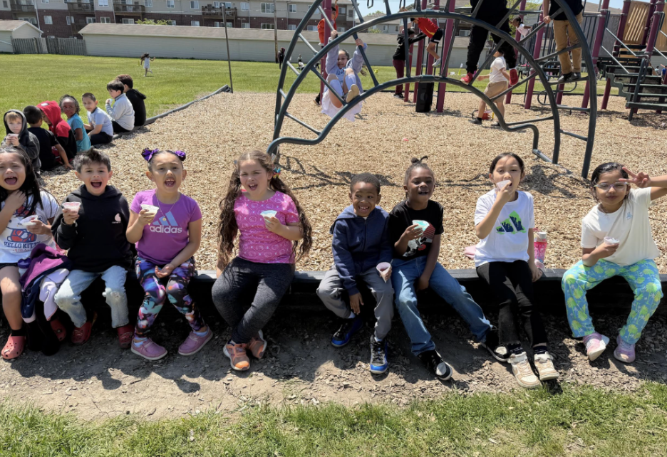 Students enjoying ice cream cones seated next to the school's  playground on a sunny day