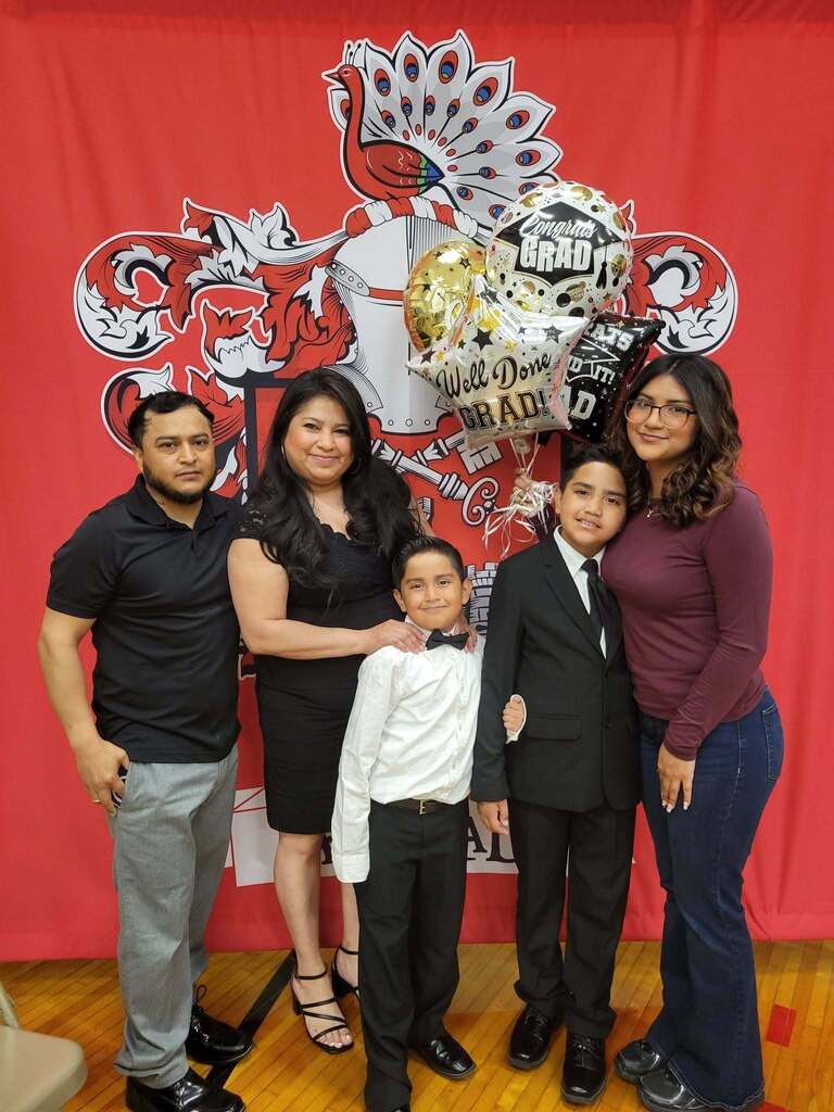 smiling family of five posing together in front of a red background with balloons during an indoor graduation ceremony