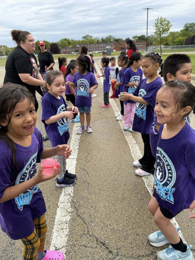 Two lines of children facing each other, smiling and playing with water balloons during a school field day event