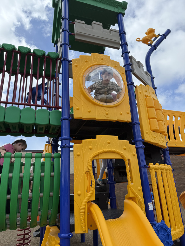 Student looking through a glass playing on the outdoor playground set at YMCA