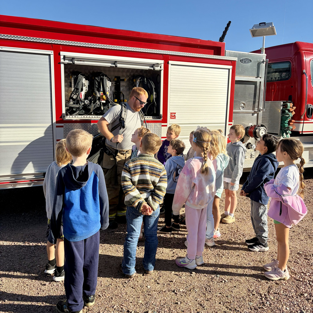 First grade class watches as the firefighter shows him his gear he uses in a fire.