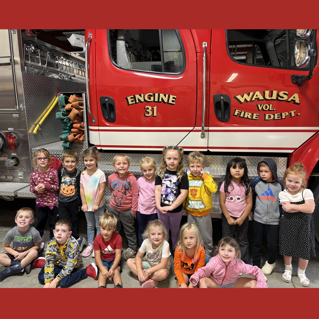 The preschool class is sitting in front of the fire engine after their tour of the facilities.