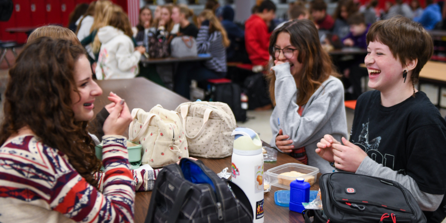 Four female students laugh while sitting at a lunch table at Wauwatosa East High School.