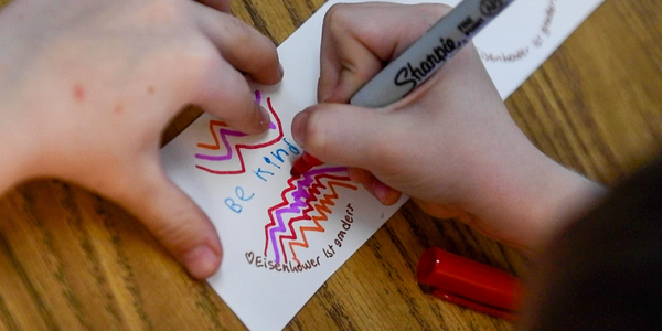 student's hands writing be kind on a sticker