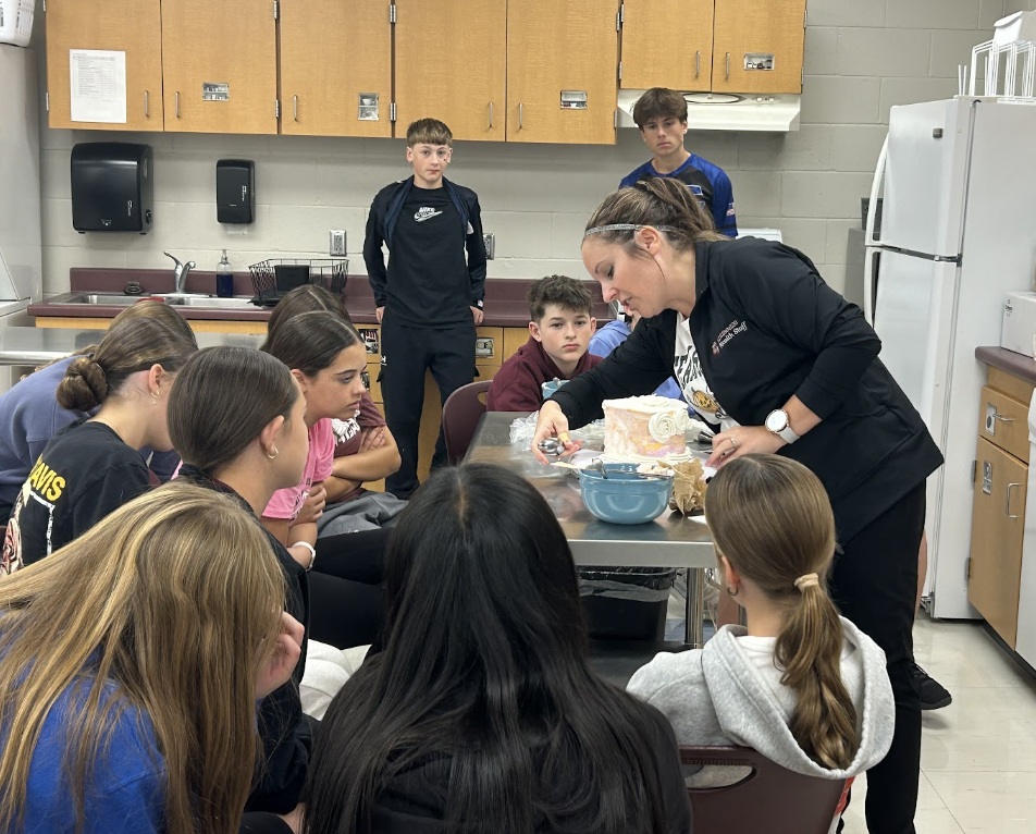 Sami demonstrates for the students how to create different textures on a cake with frosting. 