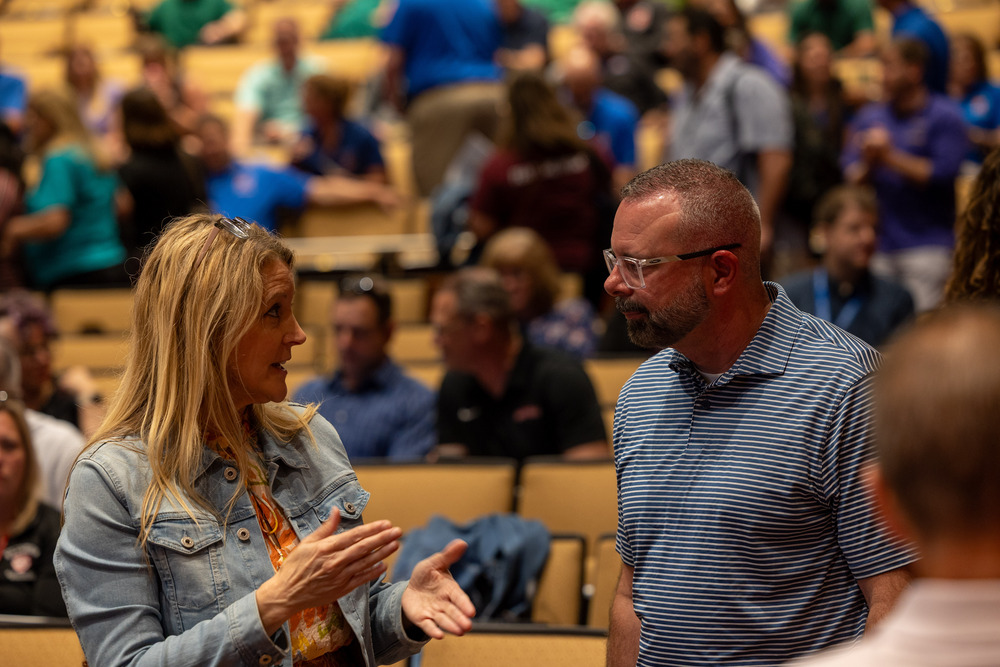 A woman and a man talk in a crowded auditorium