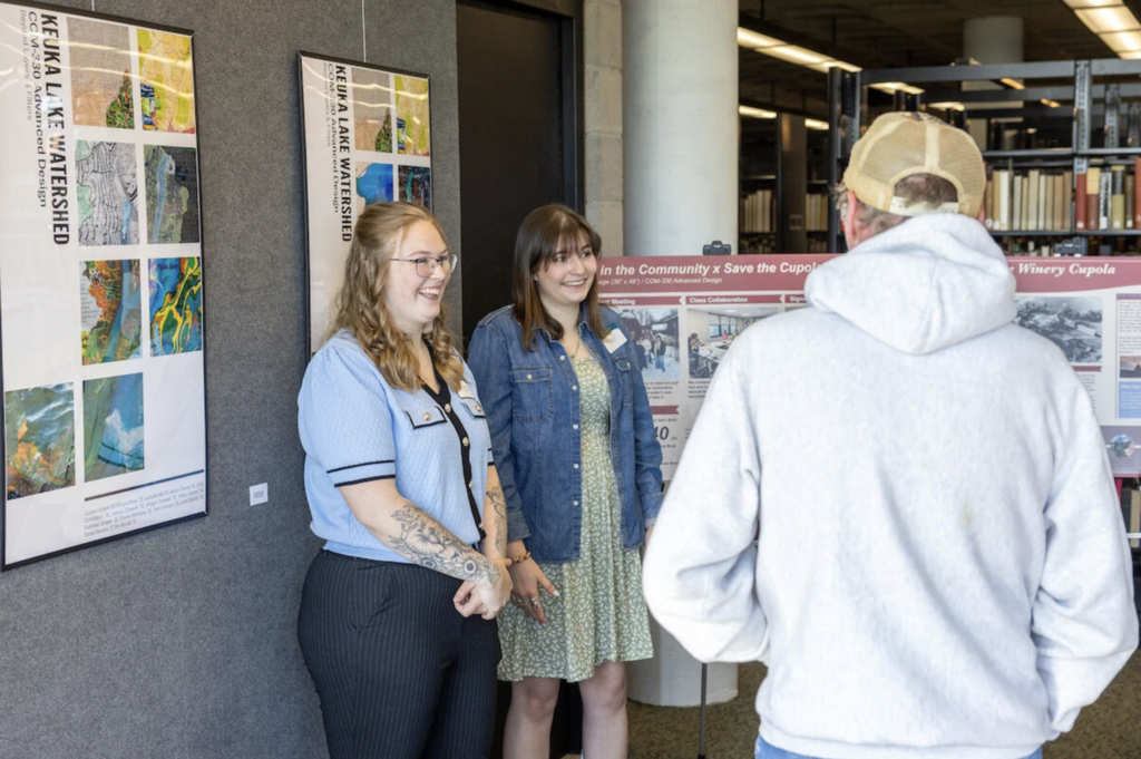 Two young women present a project while smiling in front of a posterboard.
