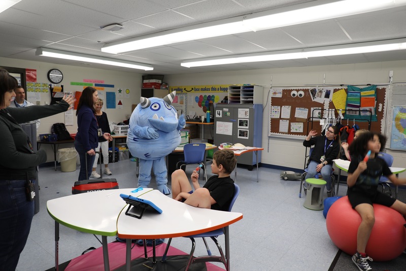 A monster mascot visits a classroom of children and teachers