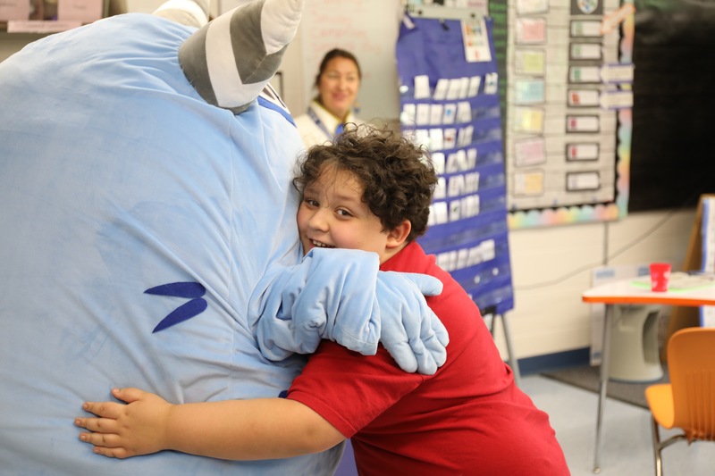 A boy hugs a monster mascot from a learning program students use