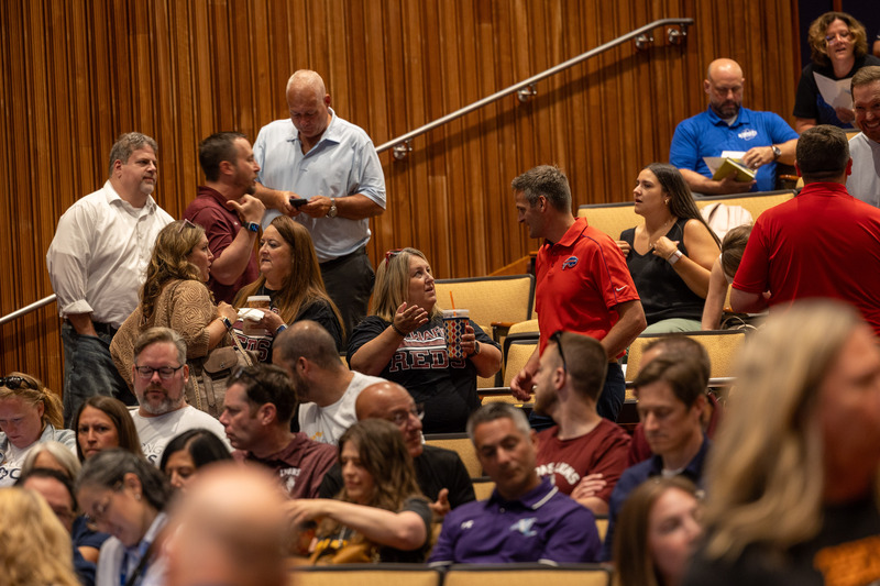 A group of adults mingle in a crowded auditorium.