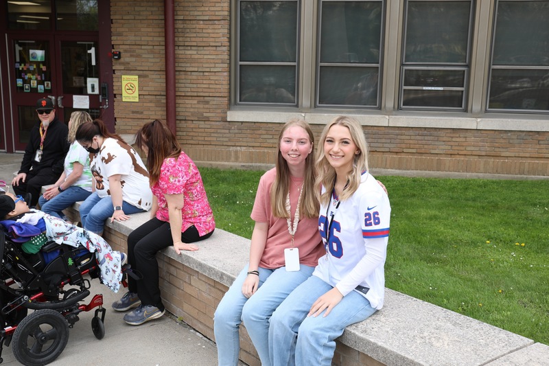 Two female students sitting outside smile for a photo