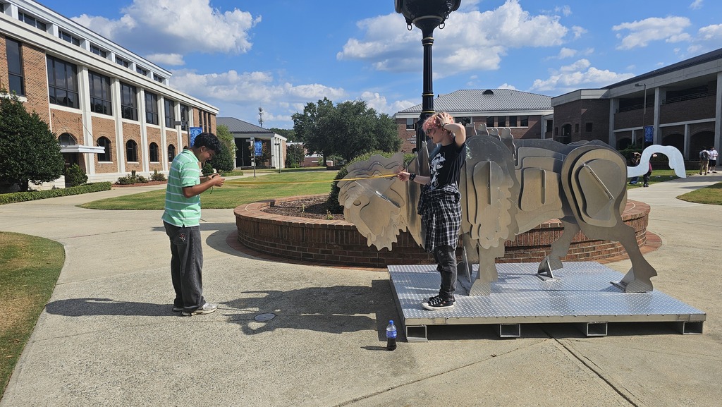 Two students measuring right angles outside on the WCC campus with the bison statue.