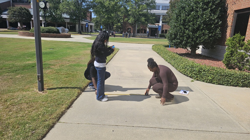 Two students measuring right angles on the sidewalk outside.