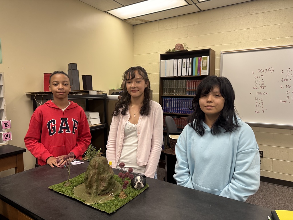 Three students with their model volcano standing in a classroom.